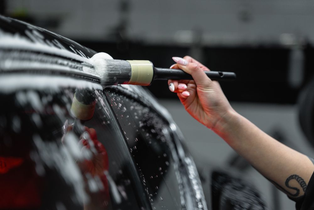 Detailing brush working foam along a car's window trim