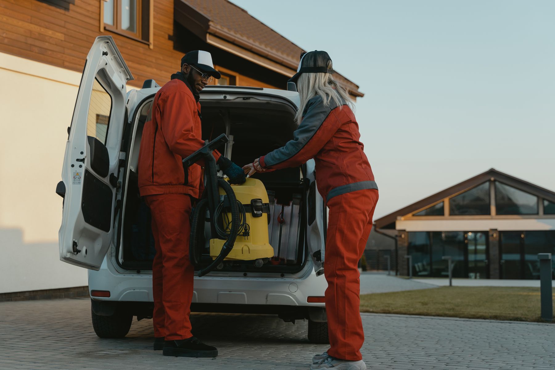 Two uniformed technicians unloading a cleaning machine from their van outside a home