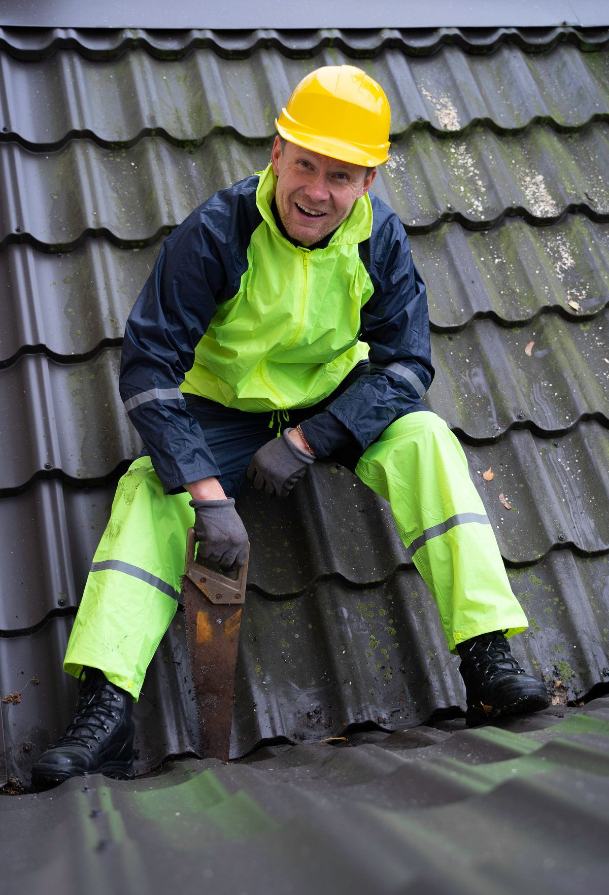 Smiling roof tech in a hard hat and hi-vis rain gear sitting on a roof