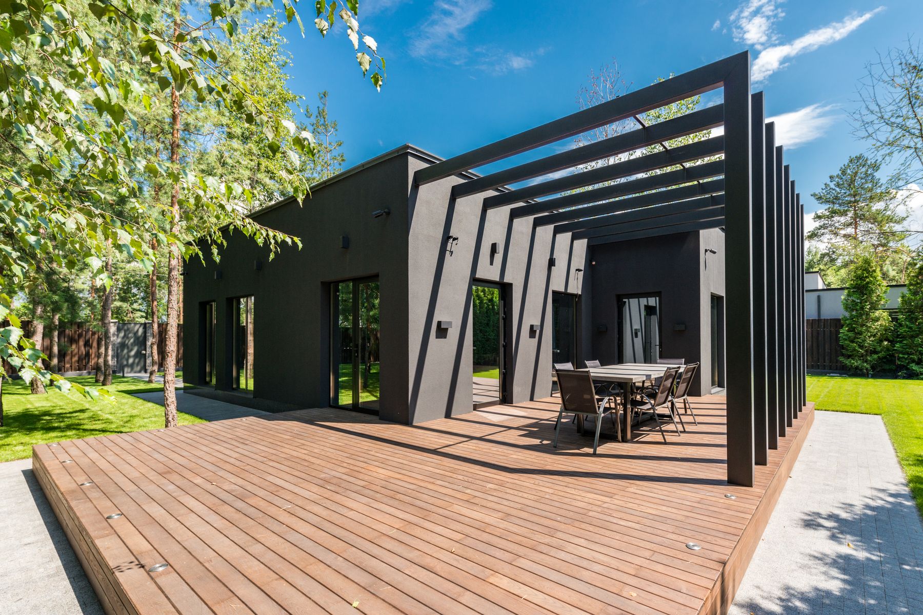 Freshly stained wood deck beside a modern black house and pergola