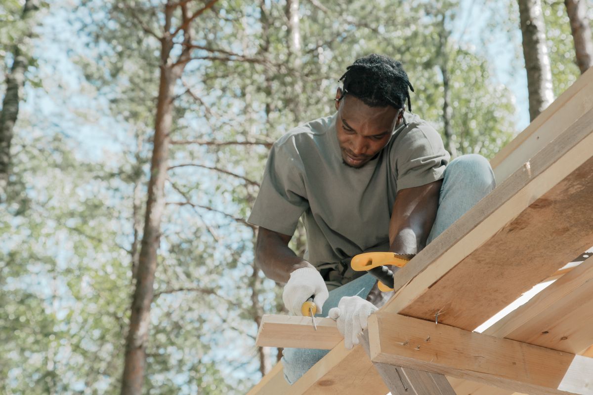 Carpenter cutting a wooden beam with a hand saw outdoors