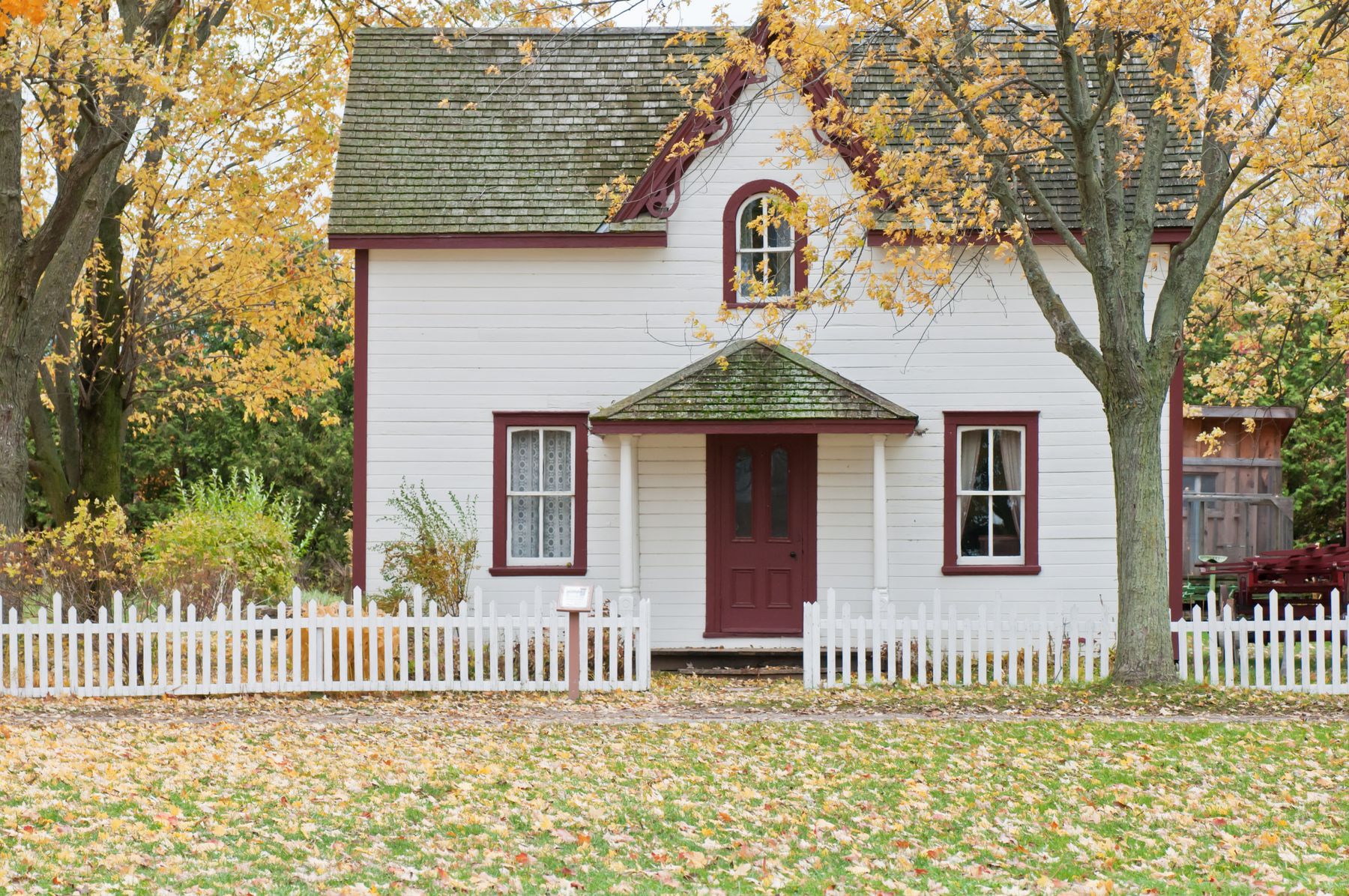 White farmhouse with red trim and fallen leaves across the lawn