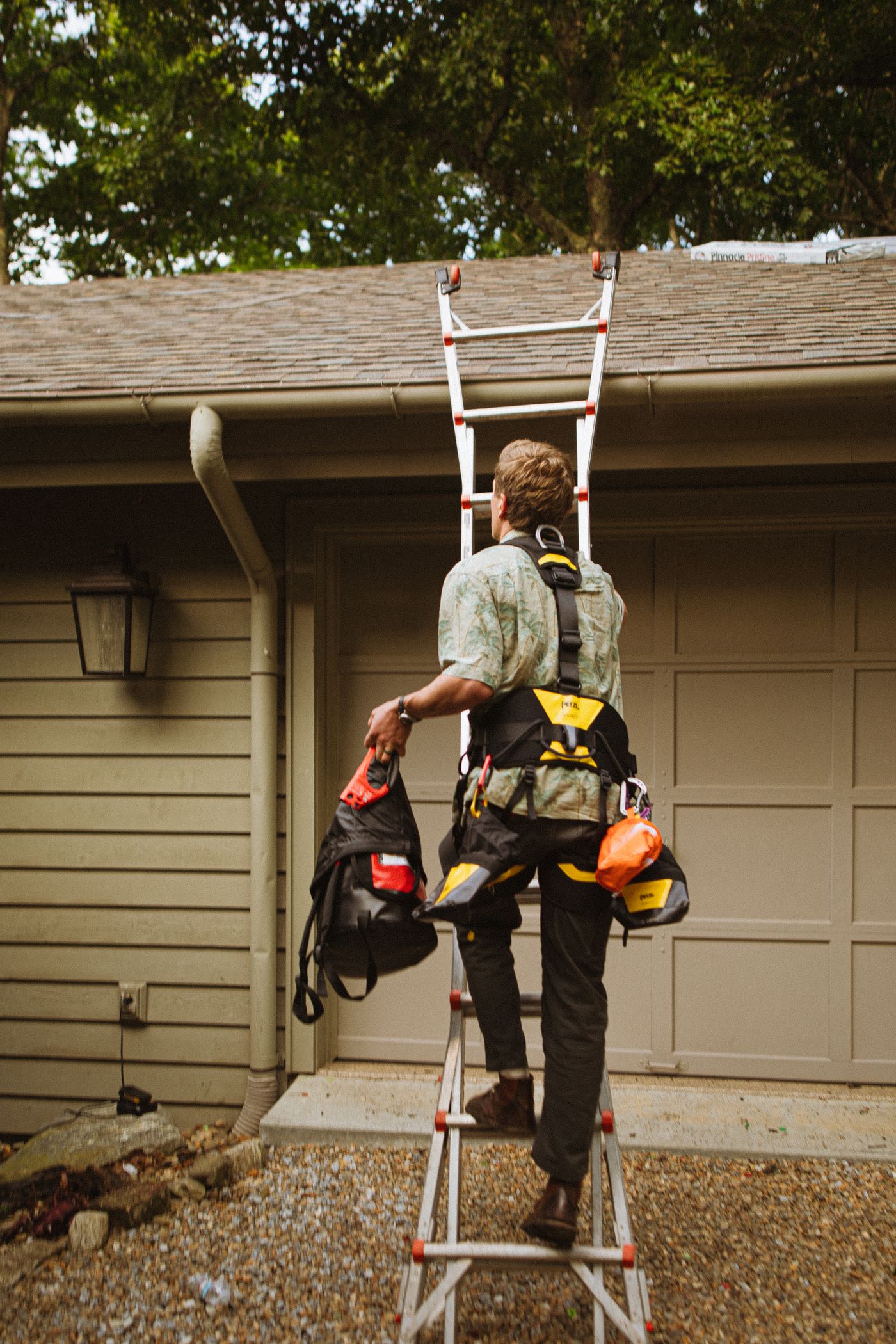 Technician in a safety harness climbing a ladder to a garage roofline
