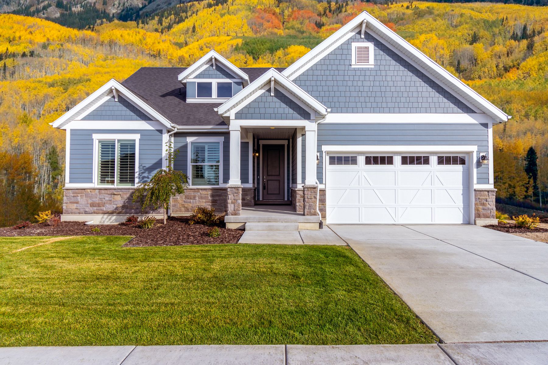 Blue craftsman house with a clean roofline and autumn trees behind it