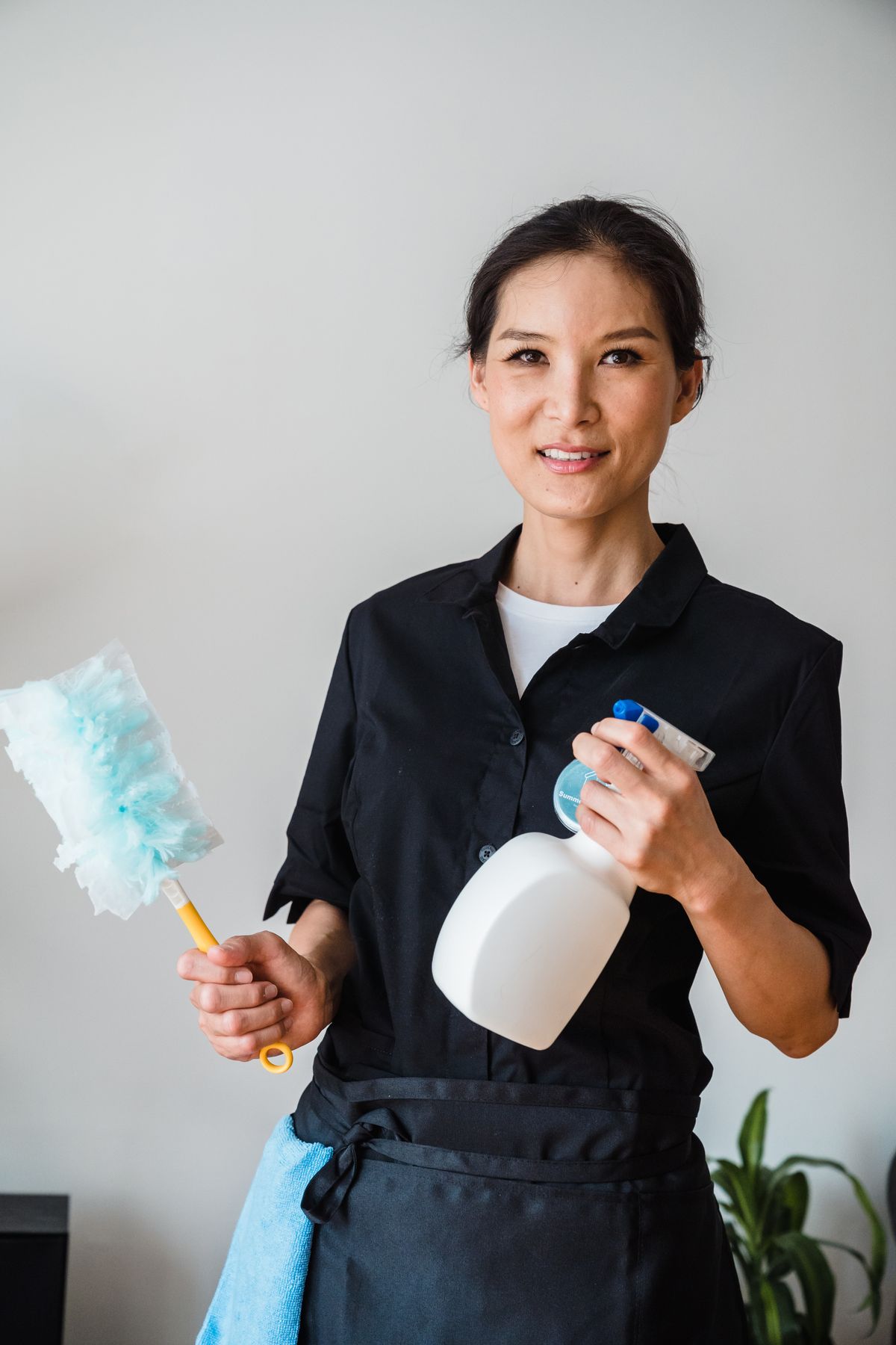 Smiling cleaner in a black uniform holding a duster and spray bottle