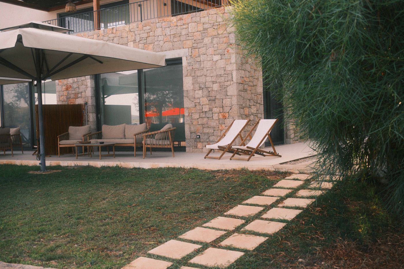 Stone house terrace with loungers and a stepping-stone path across the lawn