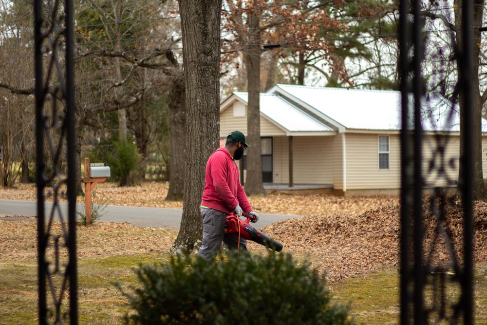 Crew member blowing fallen leaves off a front yard