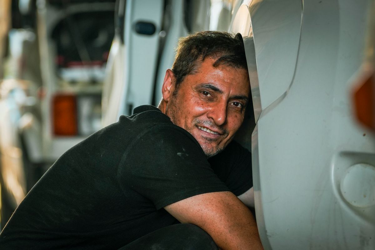 Smiling mechanic leaning against a vehicle during a repair