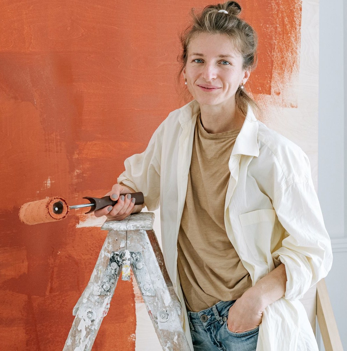 Painter holding a roller on a ladder beside a freshly painted terracotta wall