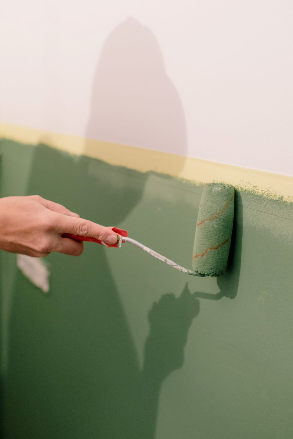 Roller laying sage green paint below a crisp tape line