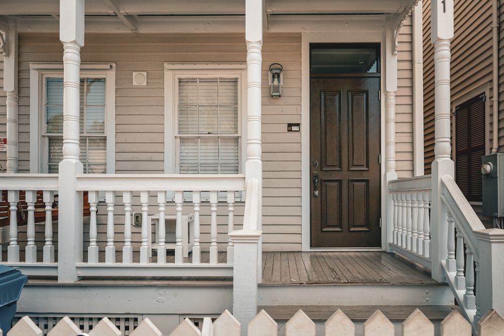 Freshly painted front porch with beige siding, white trim and a dark wood door