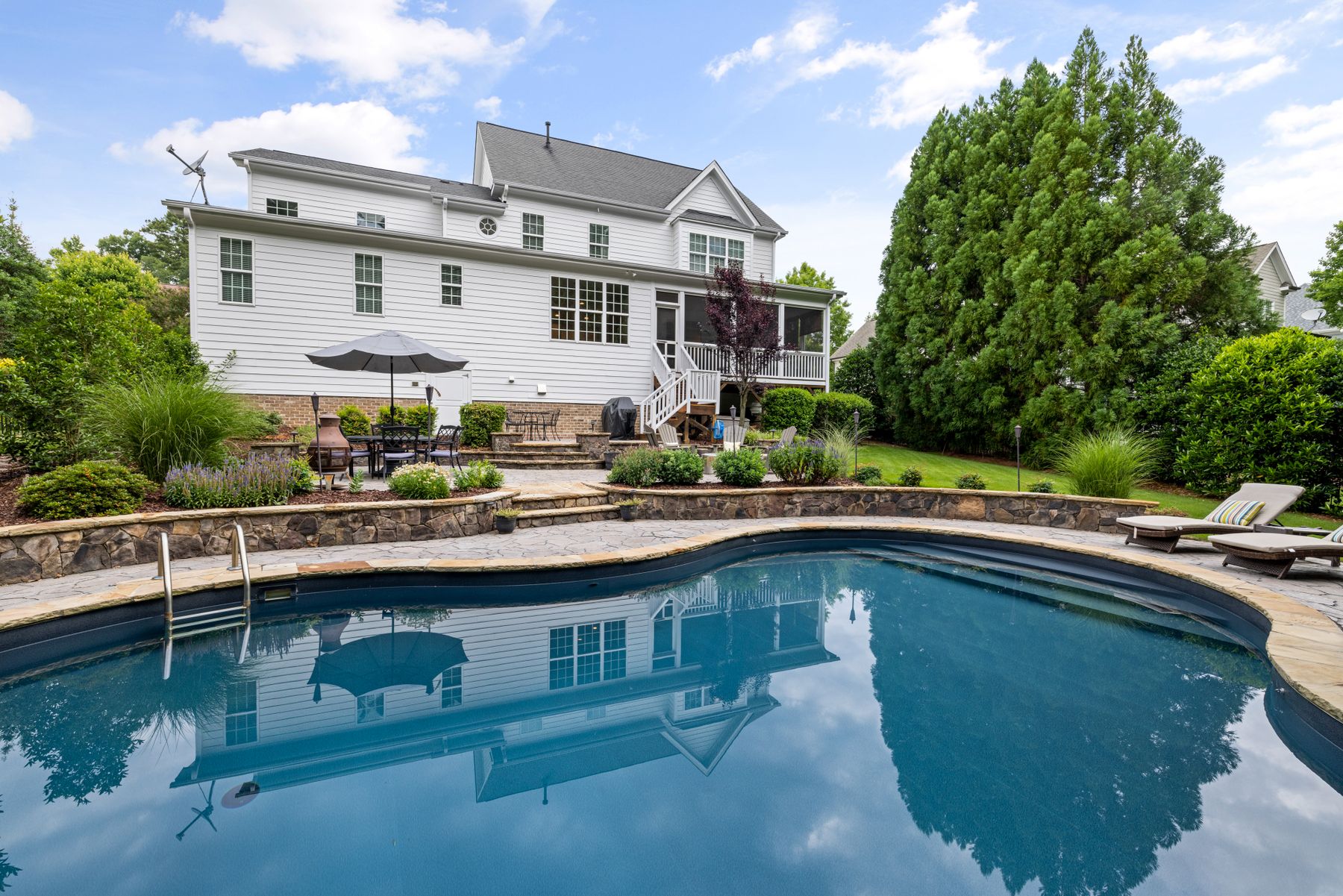 Clear kidney-shaped pool behind a white two-story home