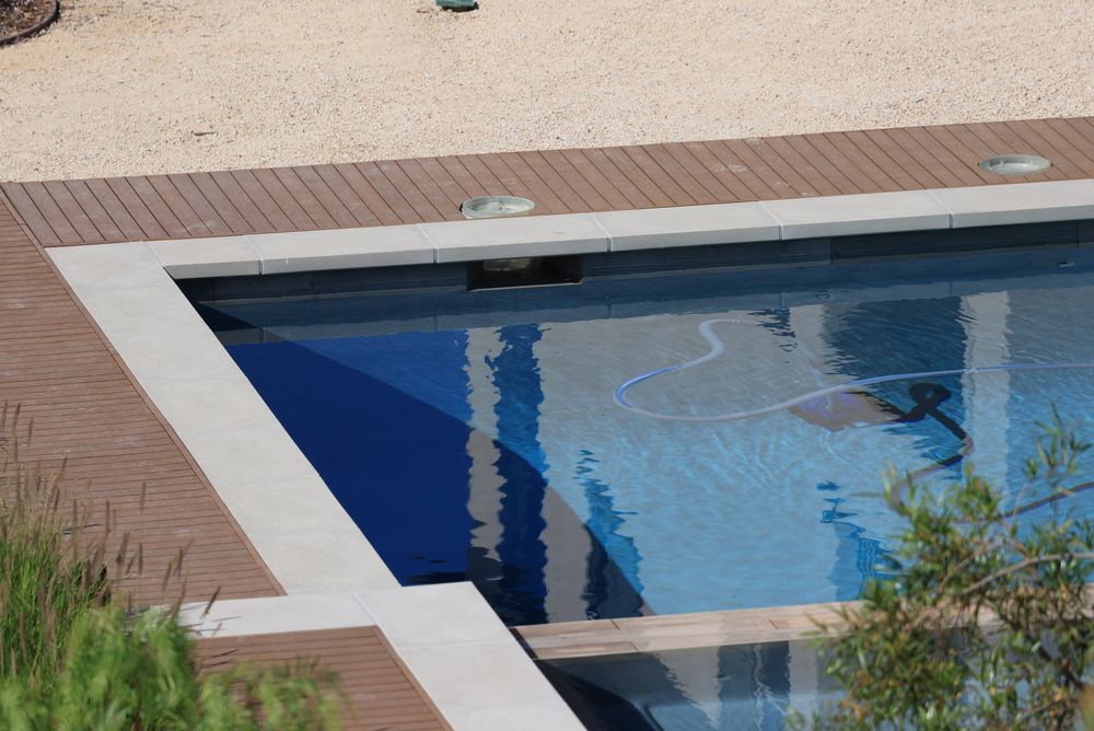 Automatic pool cleaner hose working along the floor of a clear pool beside a wood deck