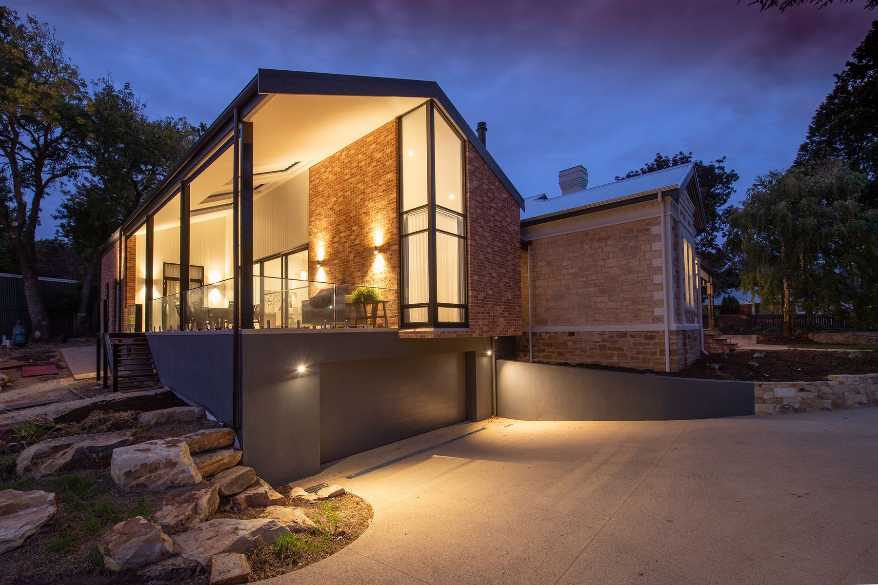 Modern home with clean stone steps and driveway lit up at dusk