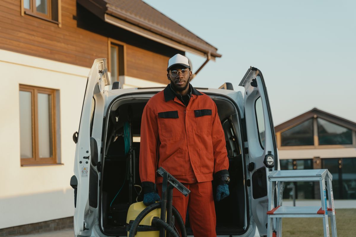 Exterior cleaning pro in an orange uniform beside his open service van