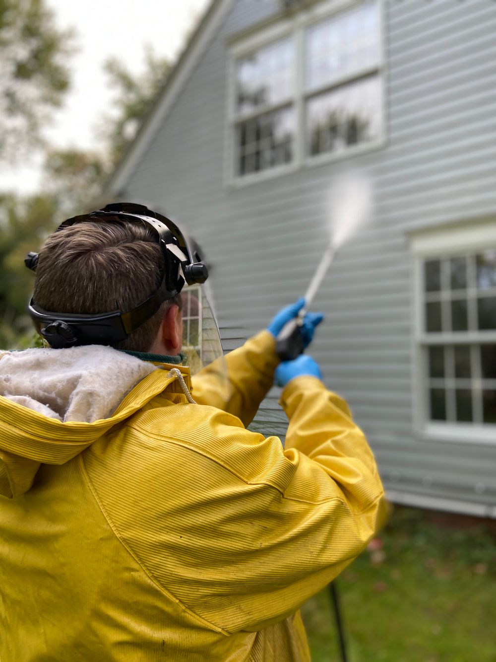 Technician soft-washing gray lap siding