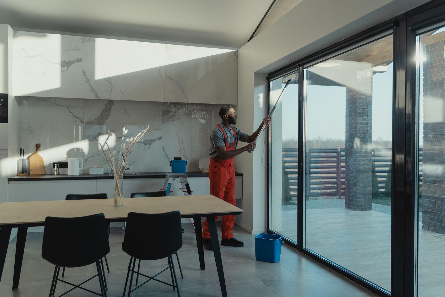 Technician in overalls cleaning floor-to-ceiling glass doors with an extension pole